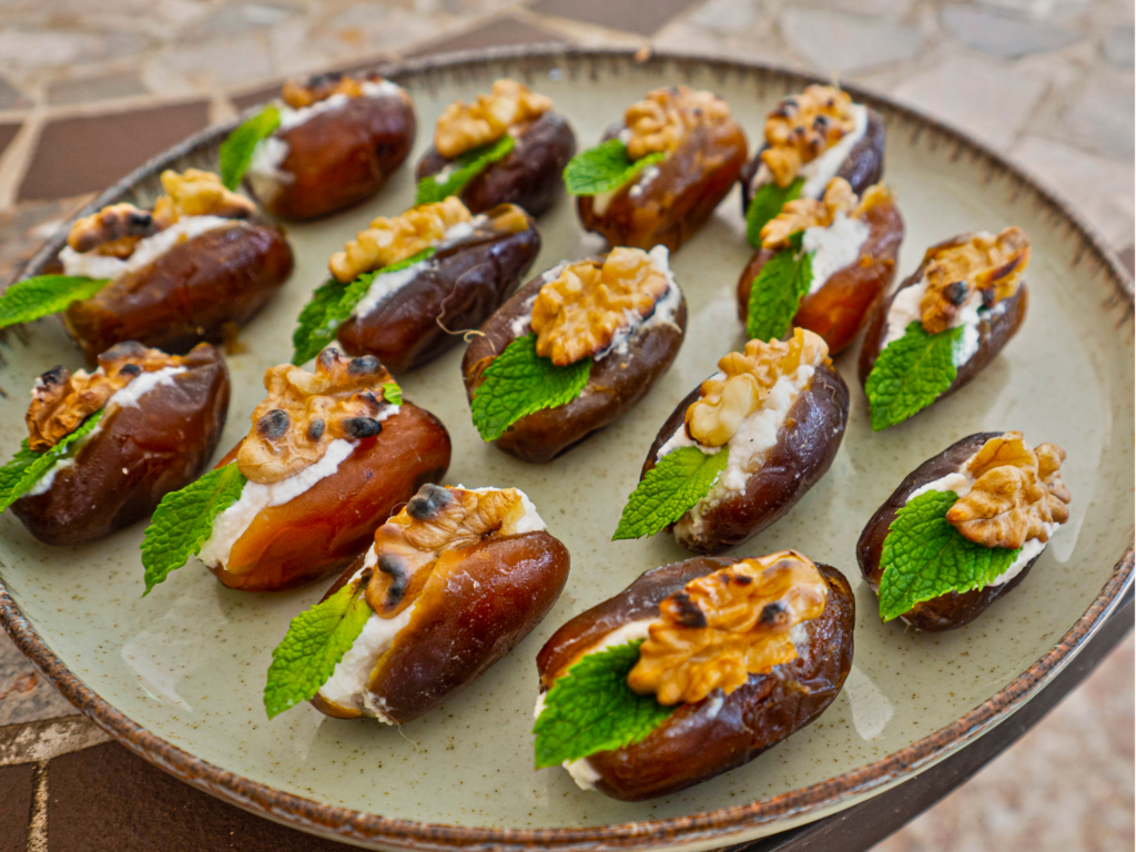 A plate of dates stuffed with cream cheese, topped with walnuts and fresh mint leaves, arranged beautifully on a rustic ceramic plate.