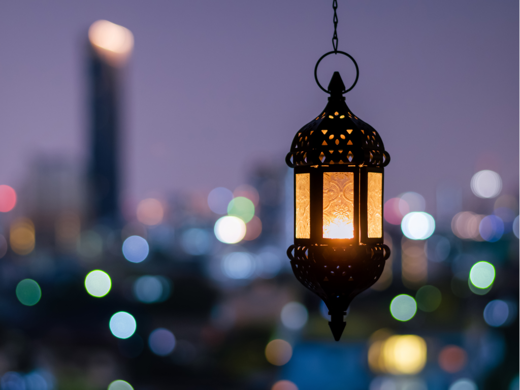 A glowing traditional lantern hanging against a blurred cityscape at night, with colorful bokeh lights in the background.