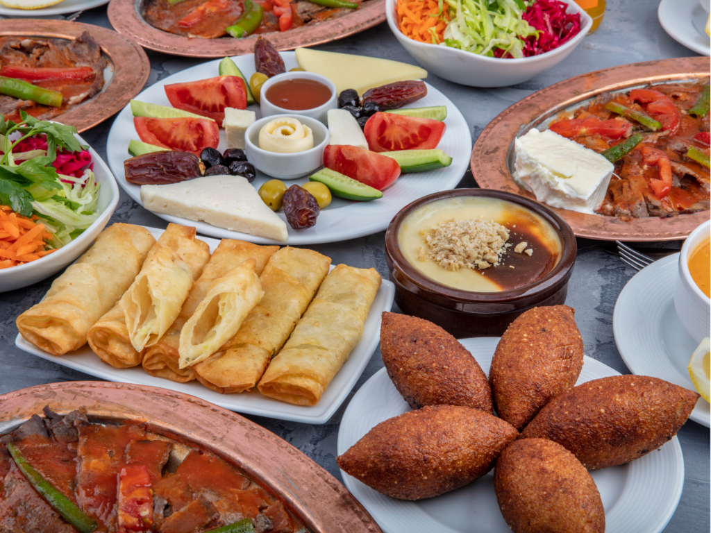 An assortment of Middle Eastern dishes including kibbeh, cheese rolls, fresh salads, dates, roasted meat, and dessert, beautifully arranged on a table.