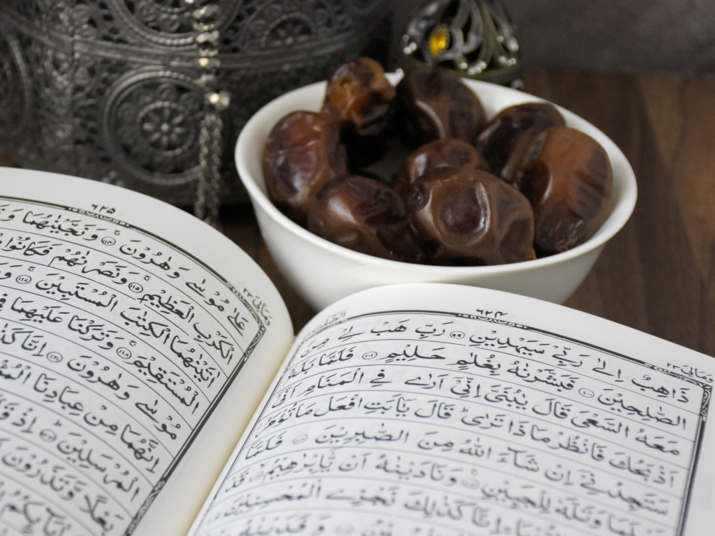 An open Quran with Arabic text beside a bowl of fresh dates, symbolizing spirituality and tradition.