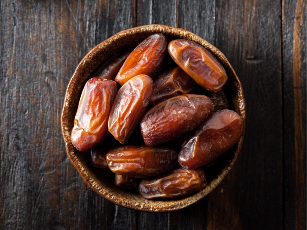 A rustic bowl filled with plump, fresh dates on a dark wooden surface.