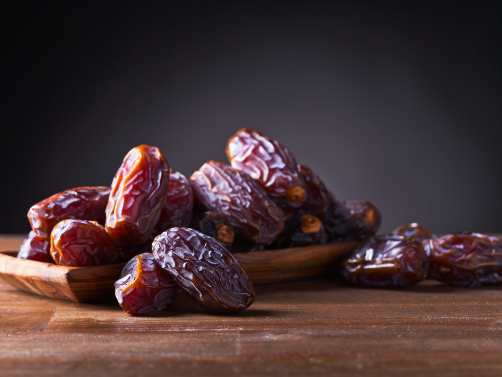 Close-up of glossy, ripe dates arranged on a wooden plate with a dark background.