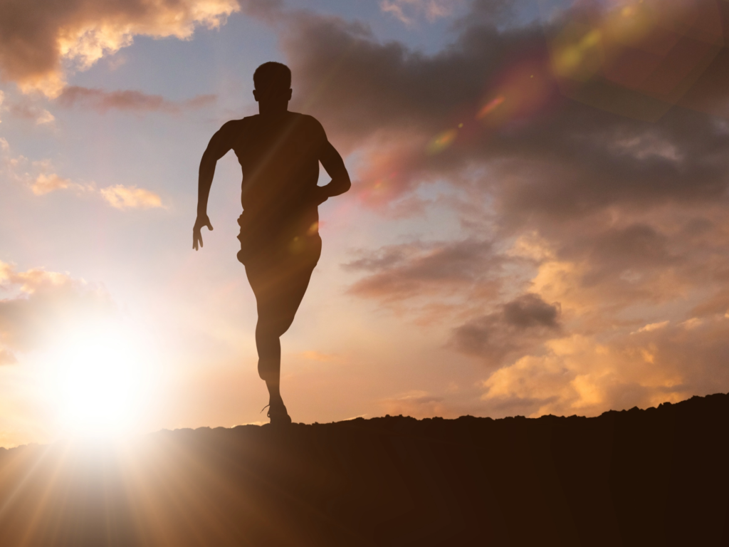 A silhouette of a man running uphill at sunrise, symbolizing energy and endurance, with golden rays of light breaking through the clouds.