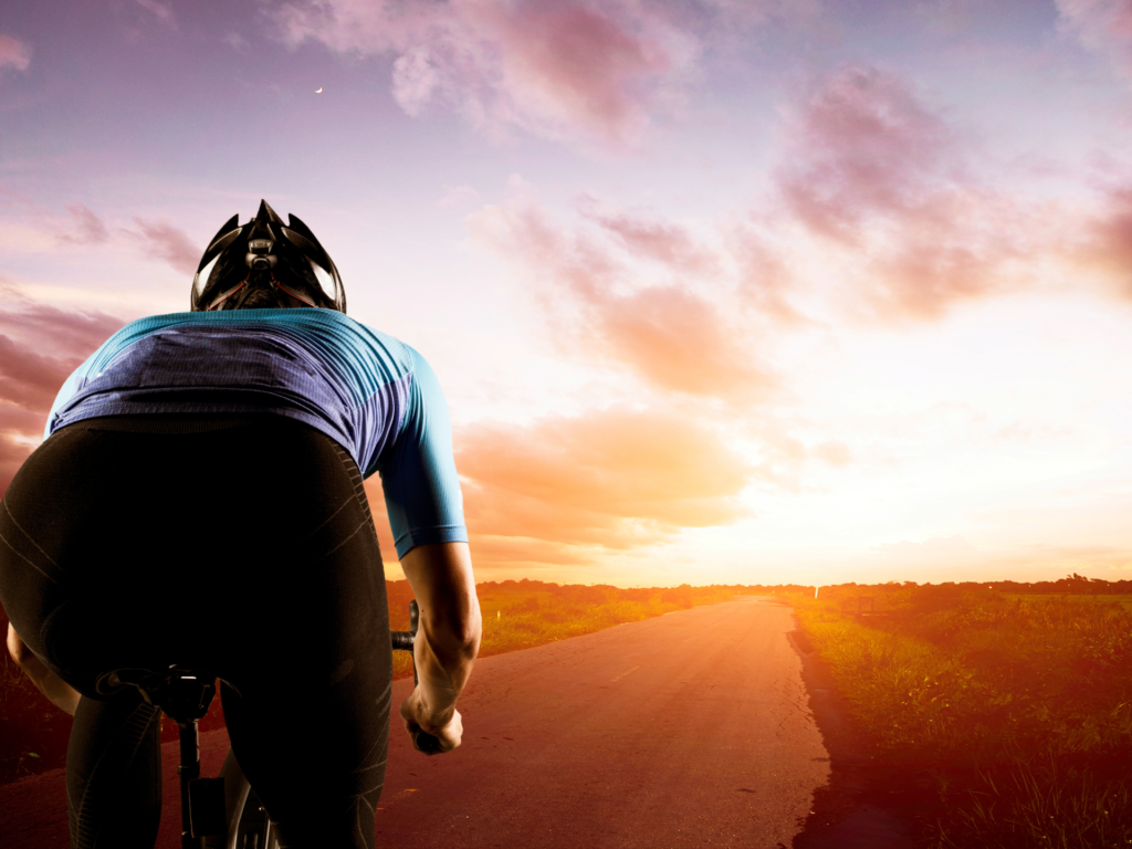 A cyclist in a blue jersey riding towards a sunset, symbolizing endurance and the importance of natural energy sources like dates for athletes.